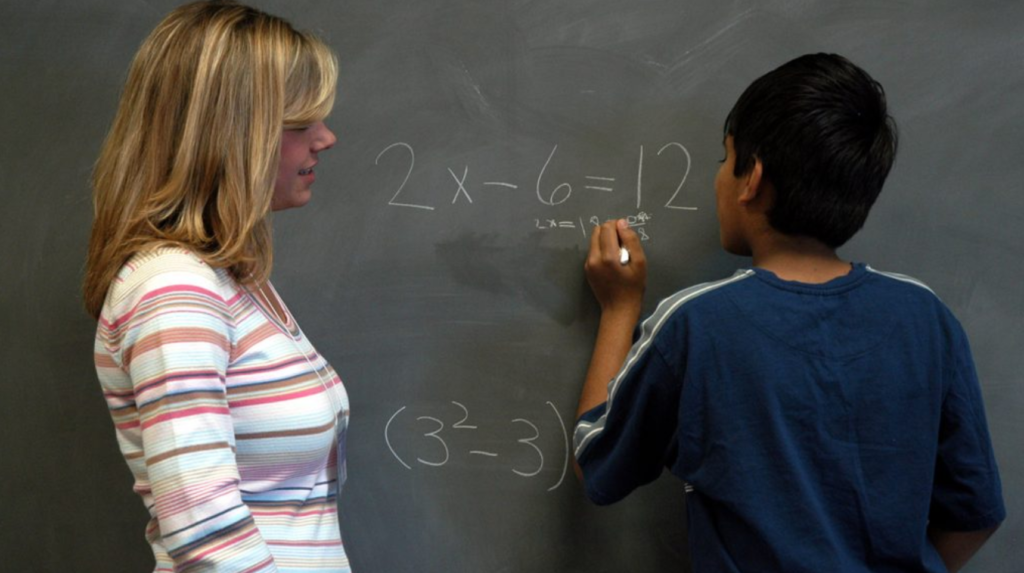 A student and a teacher doing a math problem at a chalkboard